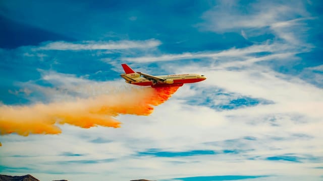 An aircraft releases fire retardant over mountains, highlighting aerial firefighting efforts.