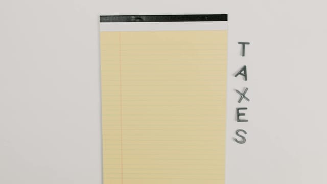 Close-up of a yellow legal pad and the word 'TAXES' on a white surface, ideal for finance themes.