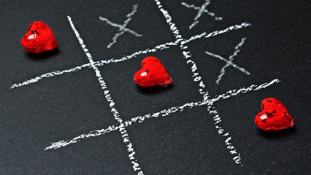 A passionate twist on tic-tac-toe with red heart pieces on a chalkboard grid.