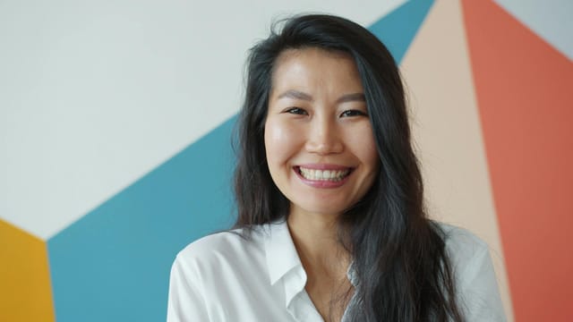 Portrait of an adult woman smiling in front of a colorful geometric wall indoors.