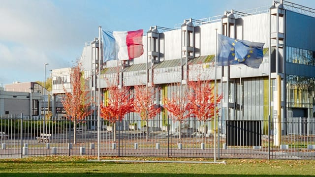 Modern building in Compiègne, France with French and EU flags, autumn trees.
