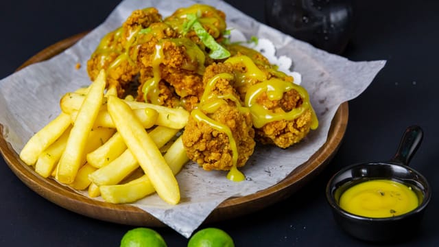 Delicious crispy fried chicken with fries, lime, and dipping sauce on a wooden platter.