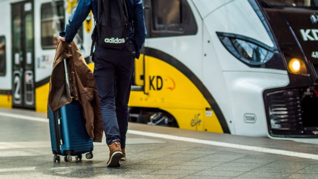 Person with suitcase preparing to board a train at a station.