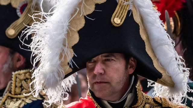 A man in an ornate Napoleonic soldier costume with a feathered hat, captured at a historical reenactment.