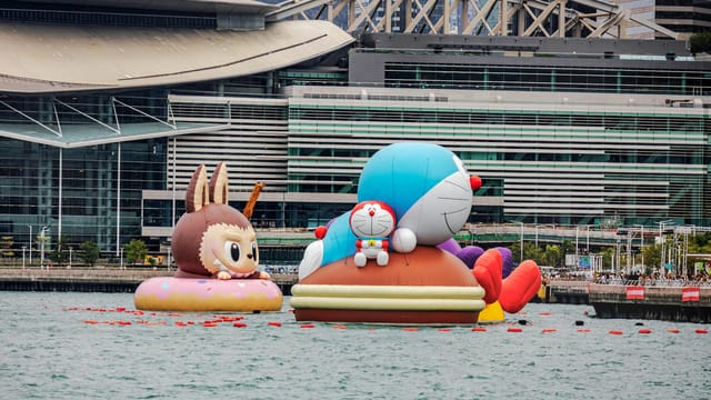 Colorful inflatable cartoon characters on display at a waterfront exhibition near a modern architectural backdrop.
