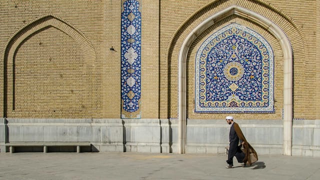 Middle-Eastern man walking past a beautifully decorated mosque wall in Qom, Iran.
