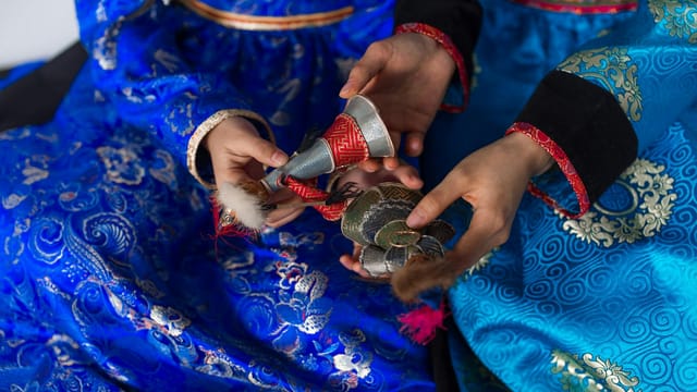 Close-up of women in blue silk kimonos holding traditional cultural figurines, showcasing intricate designs.