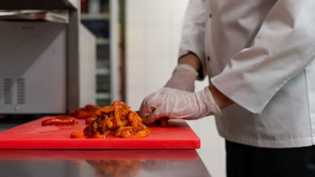 Chef chopping vegetables on a red cutting board in a professional kitchen.