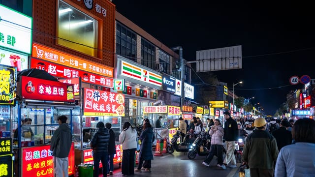 Bustling night market filled with diverse food stalls and bright neon signs in an urban street.