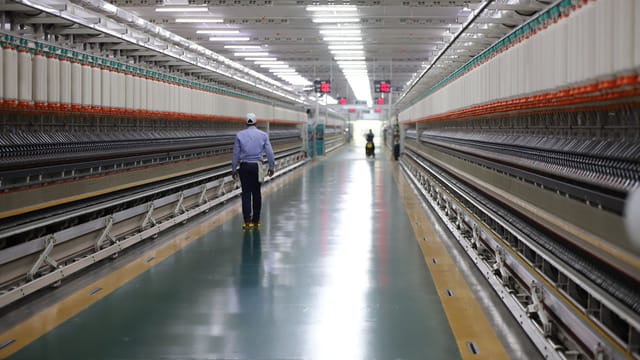 A man walks through a well-lit hallway in a modern industrial textile plant in India.