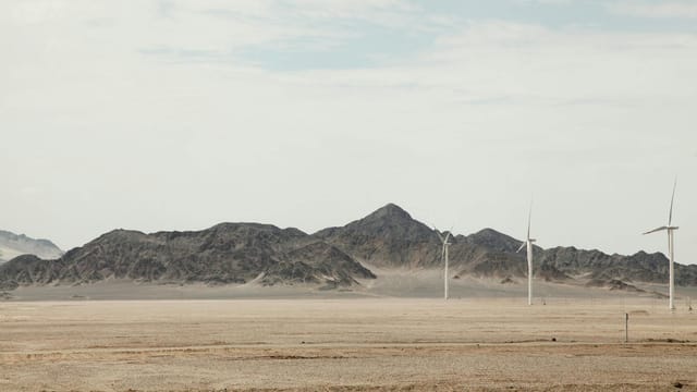 Scenic view of wind turbines in the Qinghai desert with mountains in the background.