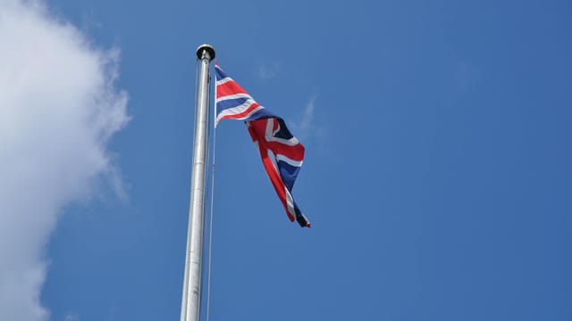 Union Jack flag waving on a flagpole against a clear blue sky in London, UK.