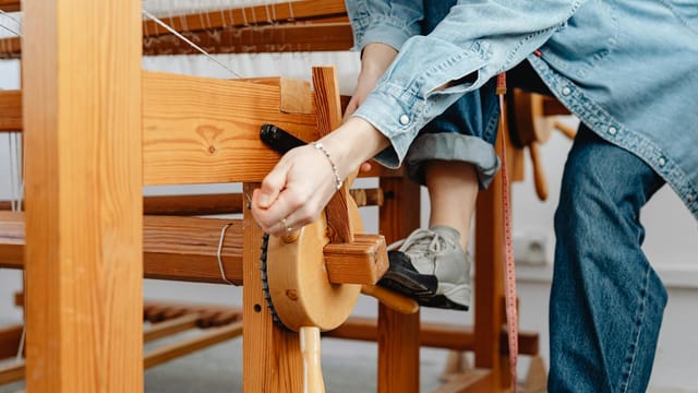 Detailed view of woman's hands weaving on a wooden loom indoors.