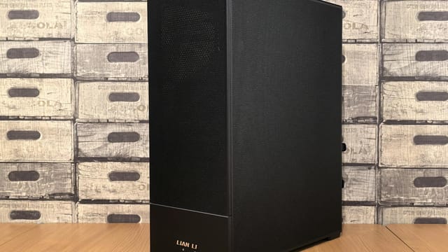 Black Lian Li computer case placed on a wooden desk with vintage box wallpaper background.