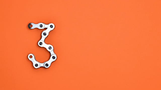 A bicycle chain forms the number three against a vibrant orange backdrop, offering ample copyspace.