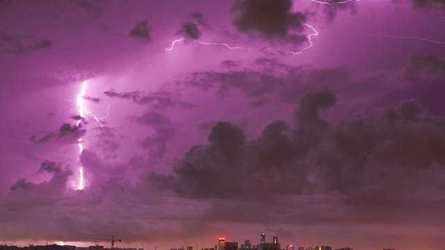 Lightning streaks illuminate the night sky above Guangzhou's cityscape, creating a dramatic scene.