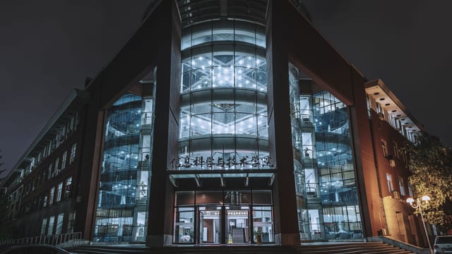 Illuminated modern building facade with glass features captured at night in an urban setting.