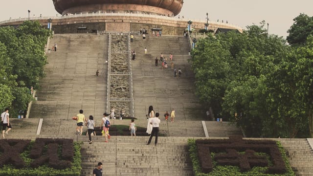 Tourists ascend the grand stairs leading to the Tian Tan Buddha in an outdoor setting.