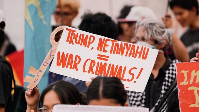Protesters hold signs at a rally, expressing political views and dissent.