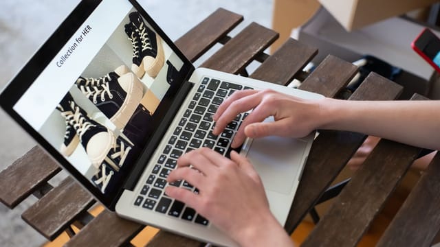 Hands of a person browsing a Collection for HER on an online shoe store using a laptop.