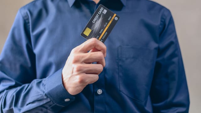 Close-up of a man in a blue shirt holding a credit card, symbolizing finance and security.