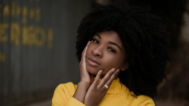 Young African American female looking at camera and thinking while standing on street near wall