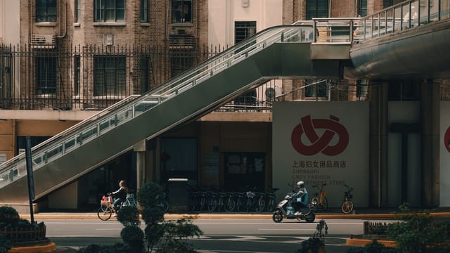 Street view in Shanghai showing an escalator, bicycles, and people in motion.