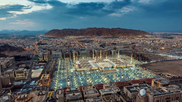 A stunning aerial view of Al-Masjid an-Nabawi in Medina at dusk, showcasing its illuminated grandeur.