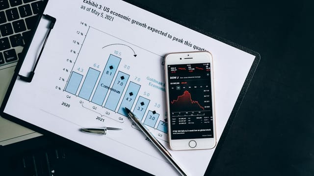 A smartphone displaying stock data rests on a financial report graph.