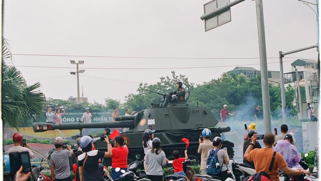 A busy street scene in Vietnam featuring a military tank and onlookers.