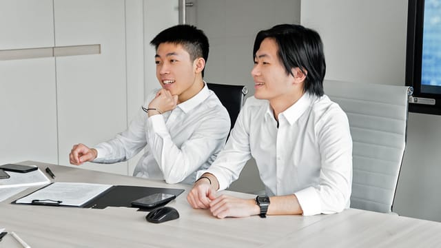 Two Asian men smiling and collaborating in a bright modern office setting.