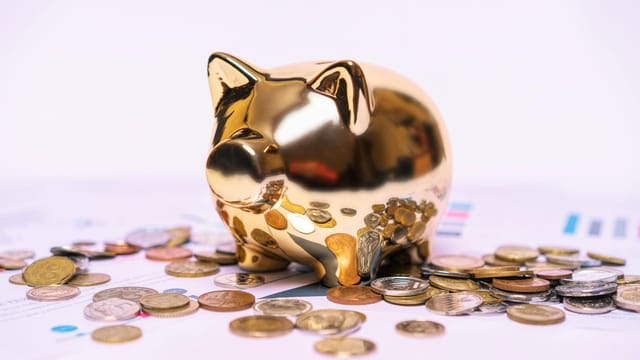 Shiny golden piggy bank on financial documents with scattered coins symbolizes savings.