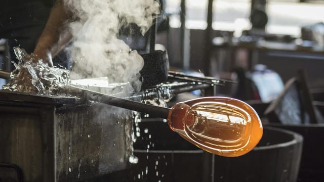 A skilled artisan involved in the intricate process of glass blowing, highlighting craftsmanship.