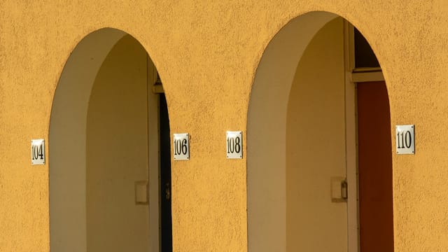 Close-up of yellow arched walls with apartment numbers in an urban setting.