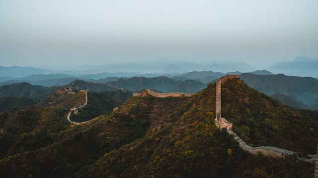 Scenic aerial view of the Great Wall of China stretching across rugged hills at dusk.