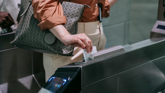 Close-up of woman using ticket at subway entrance turnstile, showcasing modern public transport system.