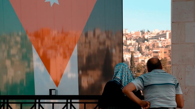 Couple observing Amman's cityscape with Jordanian flag forefront.