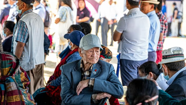 Elderly veterans gather in Aldershot, UK for a Veterans Day celebration outdoors under a tent.