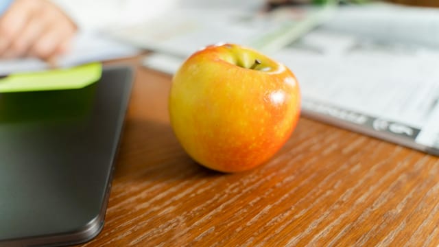 A ripe apple sits on a wooden desk beside a laptop, conveying a healthy work environment.