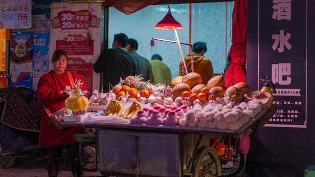 Street vendor selling fresh produce at a vibrant nighttime market.