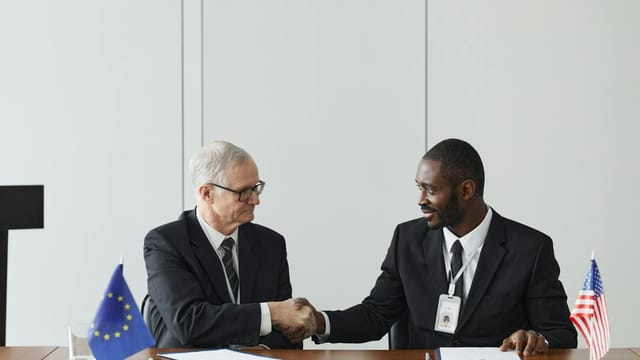 Corporate handshake between diverse businessmen representing EU and US flags, symbolizing partnership and collaboration.
