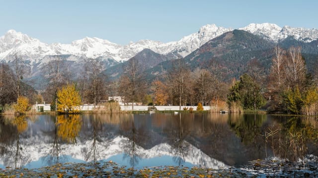 Tranquil autumn lake scene with reflections of snow-capped mountains and colorful trees.