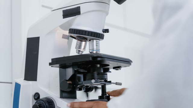 Detailed view of a scientist operating a microscope in a laboratory setting.