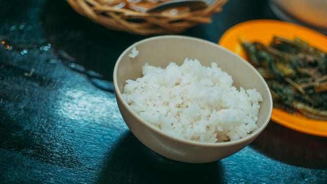 A close-up shot of a bowl of white rice with sautéed vegetables on the side, ideal for food blogs.