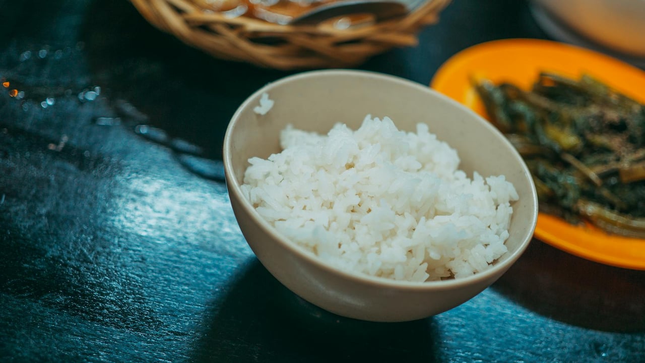 A close-up shot of a bowl of white rice with sautéed vegetables on the side, ideal for food blogs.