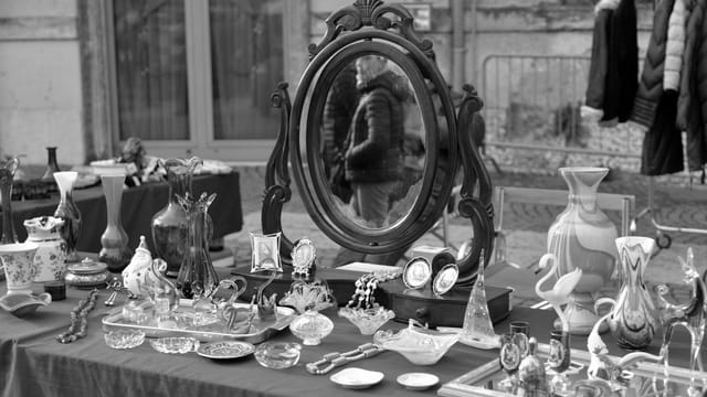 A black and white view of an outdoor antiques market with various vintage items on display.