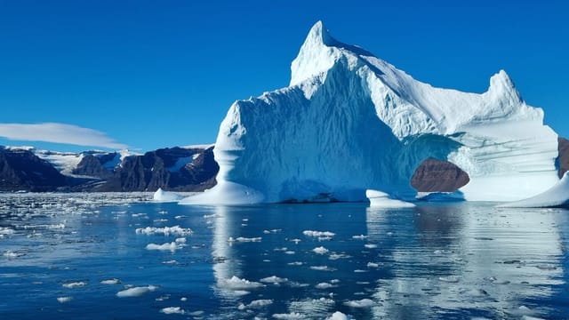 A stunning view of a large iceberg with calm arctic waters and mountains in the background.