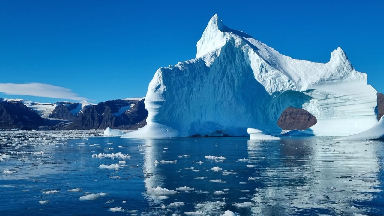 A stunning view of a large iceberg with calm arctic waters and mountains in the background.