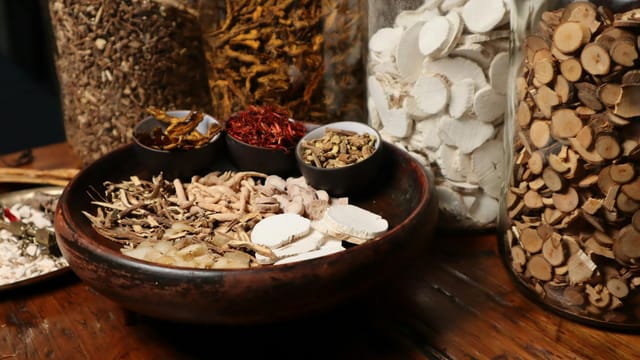 A collection of assorted traditional Chinese herbs and spices in jars and bowls.
