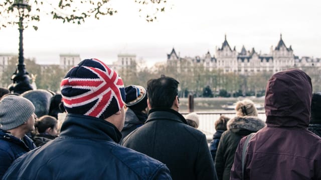 A crowd in London faces iconic architecture. Prominent British Union Jack hat in focus.